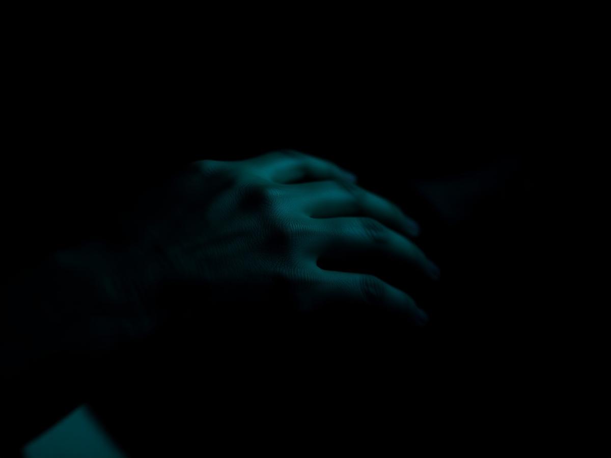 A caregiver's hand resting over an older person's hand in low teal light